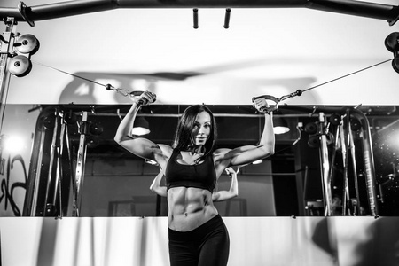 可弯曲的肌肉在健身房中电缆机上的女人。在二头肌锻炼