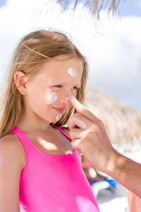 父亲对女儿的鼻子应用防晒霜。可爱的女孩，在防晒霜中的肖像