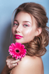 浪漫的年轻女人，与粉红色的花，看着相机在蓝色背景上的肖像
