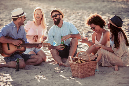 快乐的年轻人在沙滩上玩吉他。夏天, 人, 友谊, 乐趣和假期概念