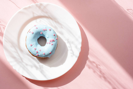 甜甜圈覆盖着蓝色的釉面, 洒上粉红色的白色盘子上的小粉红色的心在自然光线下