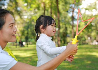 可爱小女孩和母亲玩泡沫在公园里