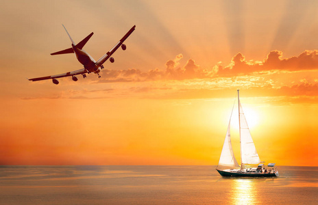 帆船航行在开阔的大海与日落背景和飞机在天空中照片