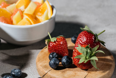 木板上的草莓和蓝莓与柑橘类水果的碗