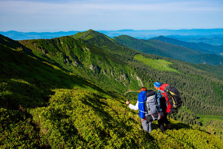 冒险家与背包站立在绿色山山脊和敬佩山的全景在他们面前。史诗般的旅行在山上。后退视图