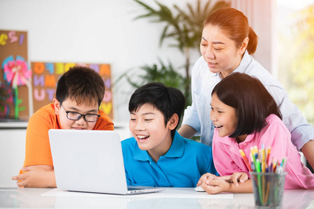 亚洲女教师和可爱的亚洲儿童一起使用笔记本电脑