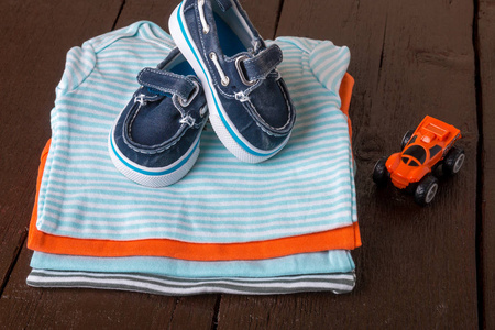 折叠船鞋的蓝色和橙色紧身衣裤上木制背景上。新生男婴的的尿布。婴幼儿服装堆栈。孩子的衣服。关闭