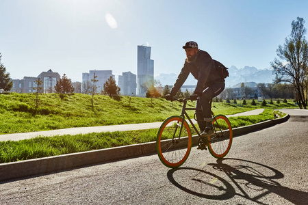 骑自行车的人骑在城市的道路上, 以绿色的草地和山脉为背景。阿拉木图市。生态运输