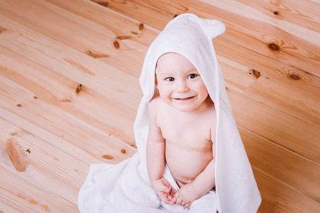 棕色眼睛的宝贝男孩是五个月大毛巾裹着白色木制背景上的耳朵