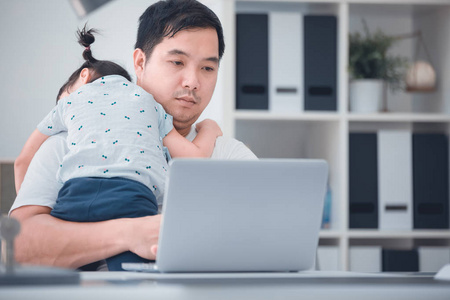 亚洲现代家庭和小女孩, 而爸爸与笔记本电脑工作表在家里办公室