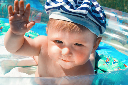好奇的快乐的十个月大的婴儿在蓝色的游泳池里摆姿势