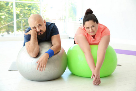 疲惫的超重男子和妇女休息健身球在健身房