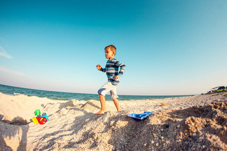 一个男孩在海滩上玩沙子。孩子沿着海岸的天空。孩子在自然开心。这个男孩是在度假