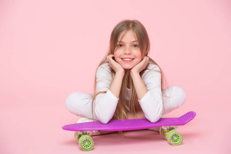 滑板的孩子躺在地板上粉红色的背景。儿童溜冰者微笑与长板。小女孩笑着溜冰板。童年的生活方式和活跃的游戏。体育活动和能量, 强力粉彩