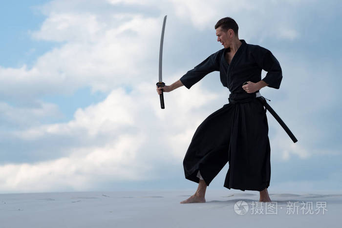 在传统的衣服, 是在沙漠中练习日本武术与日本剑-一个武士刀在日落的