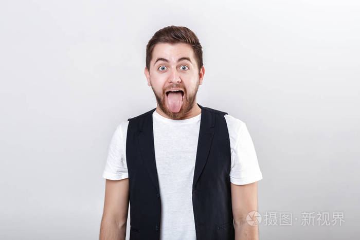 穿衬衫在灰色的背景上显示的舌头年轻黑发男人