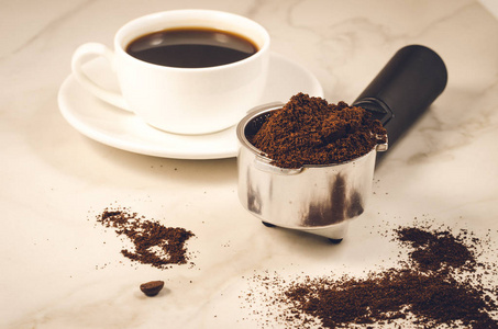 持有地面咖啡和一个白色杯持有人充满了地面咖啡和一个白色的杯子在大理石背景。选择性聚焦