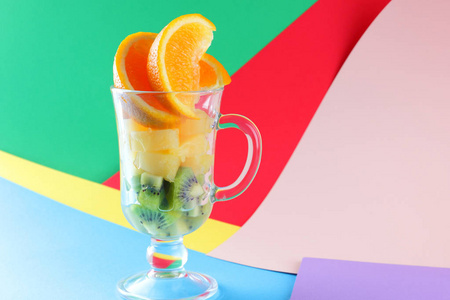 一片热带水果, 玻璃杯, 水果鸡尾酒。橘子片, 猕猴桃, 玻璃碗里的菠萝片。多色流行艺术背景, 复制空间