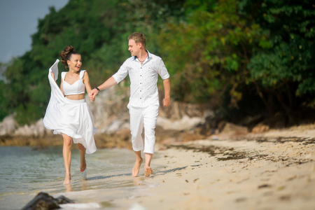 男性的新郎和女性新娘赤脚跑在海滩上照片