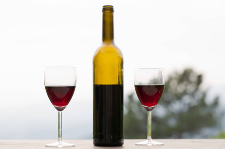 葡萄酒瓶和玻璃在木桌前，户外