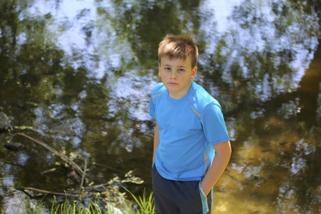 一个十几岁的年轻人在河边的公园散步时摆出一个摄影师的姿势。