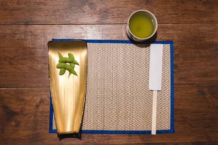 木筷在纸上盖, 煮绿豆和盐放在竹垫上的金盘子上, 杯上的热绿茶放在木桌的背景上。高级查看日本食品设备和餐厅