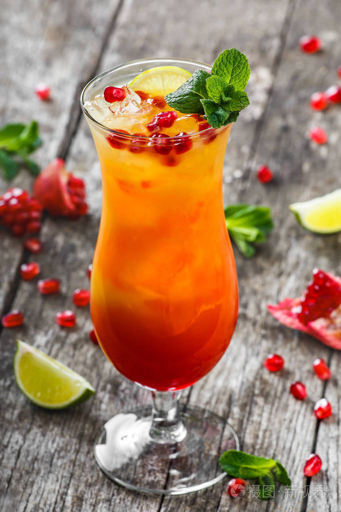 新鲜水果热带鸡尾酒与薄荷橙和木制背景上的高脚玻璃杯中的石榴夏季