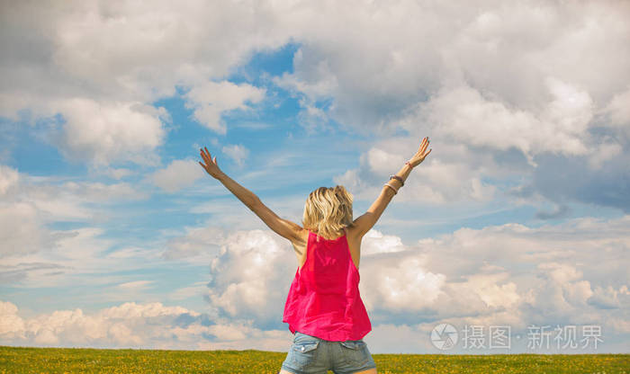 阳光明媚的日子在绿色草坪上举起双手的女人的背观