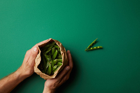 绿色表面带豌豆荚的人手持纸袋的裁剪镜头