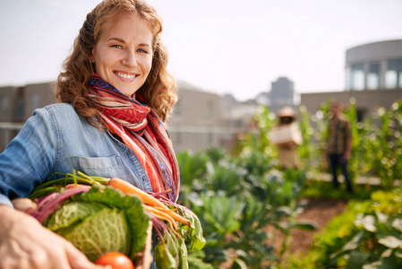 友好的女人收获新鲜蔬菜从屋顶温室花园