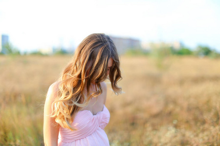 身穿粉红色连衣裙的金发孕妇在草原背景下站立