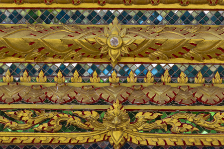 一座泰国佛寺墙上美丽的旧装饰品。镀金木图案的玻璃饰品。泰国的传统艺术。纹理特写