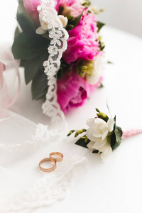 美丽的粉红色牡丹花束和结婚戒指躺在一个白色的桌子上。顶部视图