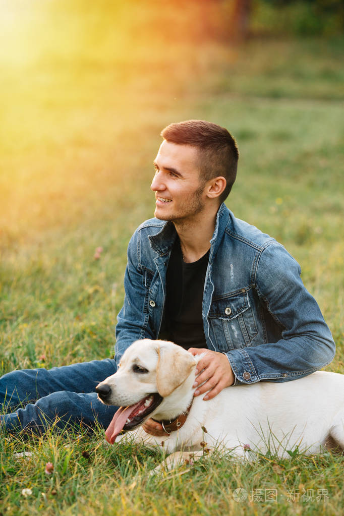 男人和狗拉布拉多在日落时分坐在草地上