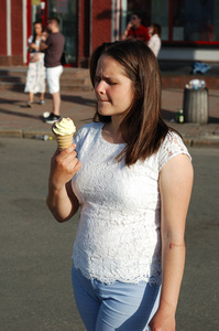 一个美丽的女孩在夏日的大街上吃着冰淇淋蛋卷。