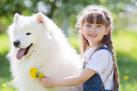 在公园里有一只大白狗的小女孩。一个美丽的5岁女孩在牛仔裤拥抱她最喜欢的狗在夏季散步