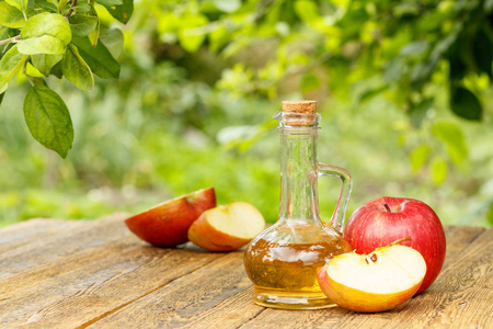 苹果醋在玻璃瓶里用软木和新鲜红苹果在老木板上, 树枝上有苹果树和模糊的绿色自然背景。