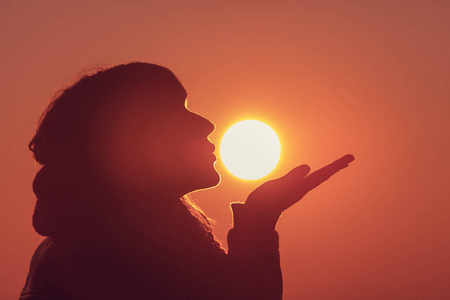 女性剪影在晚上亲吻太阳的侧面看法