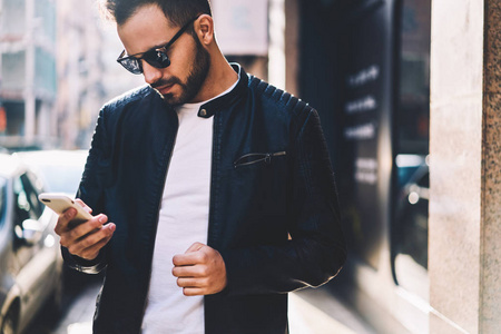 英俊的人检查在智能手机上的邮件使用时, 在城市街道上花费时间, 裁剪男性的形象时髦的服装发送短信通过手机聊天在户外网络
