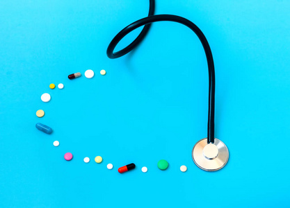 医学概念。药物听诊器和不同的胶囊和药丸形成的心脏在蓝色背景的形状。保健或疾病。医院或药房的片剂或药物