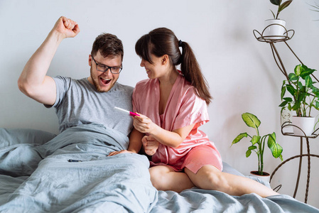 幸福的情侣在床上。妇女显示男性阳性妊娠试验