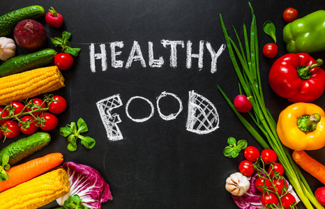 一张桌上满是新鲜蔬菜或健康食品背景的照片。健康食品概念与新鲜蔬菜烹调。标题 健康食物 是由粉笔写在黑暗背景的中间