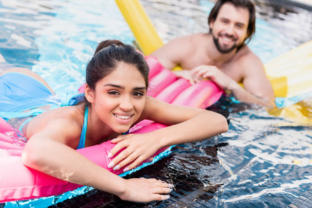 愉快的夫妇游泳在黄色和粉红色充气床垫在水池