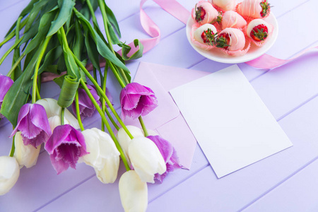 清晰的纸与信封, 草莓在巧克力, 白色和紫色的郁金香花束和粉红色丝带在丁香桌子上。为妇女或母亲的节日问候。弹簧装饰