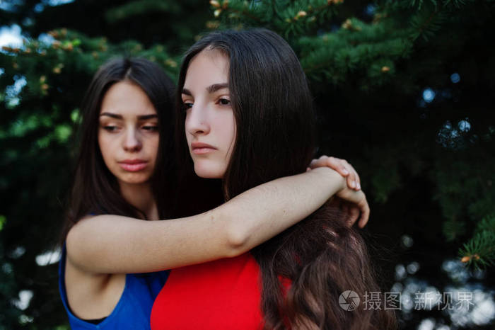两个十几岁的女孩穿着蓝色和红色的衣服摆在户外拥抱