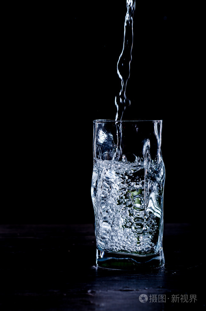 在黑色的背景上把水倒进玻璃