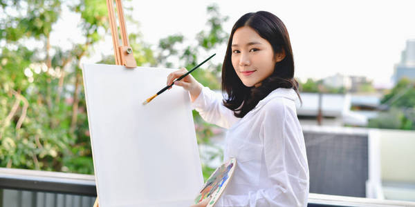 美丽的女人正在快乐地画画.房子外面的年轻艺术家绘画照片