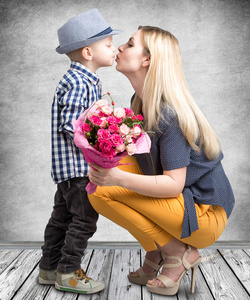 小儿子给他心爱的母亲一束美丽的粉红玫瑰，亲吻妈妈。春 妇女节 母亲节这一天