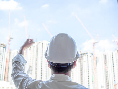 工程师人后视图身穿白色硬安全帽和白衬衫上升他的拳头与右手成功的