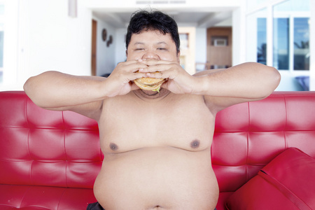 超重的人在沙发上吃汉堡